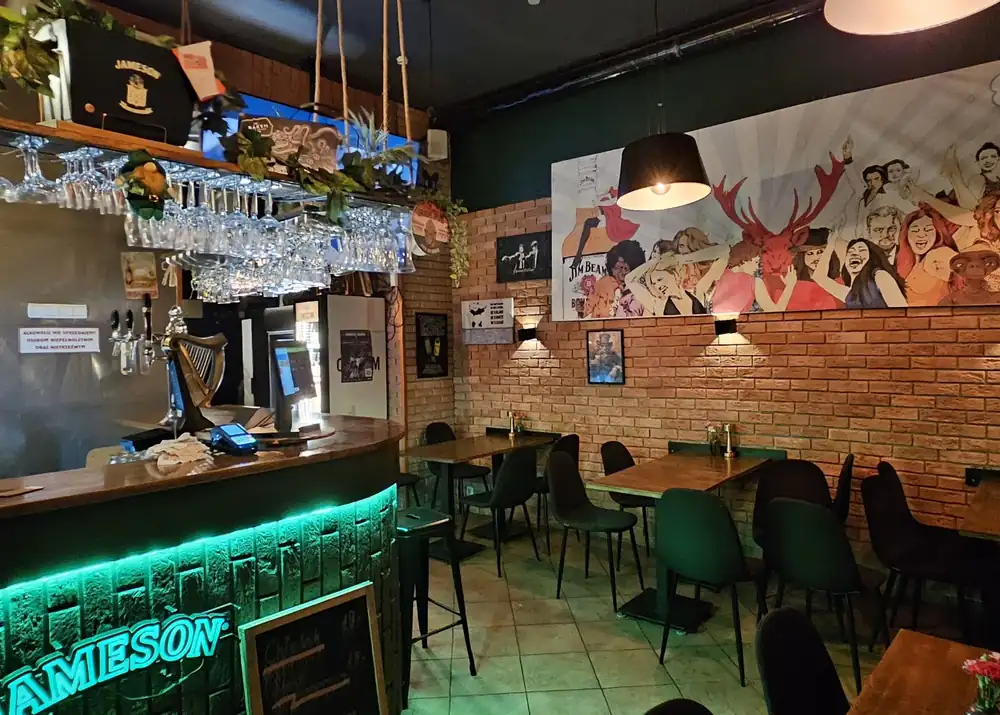 Długi bar podświetlony na zielono i stoliki w pubie