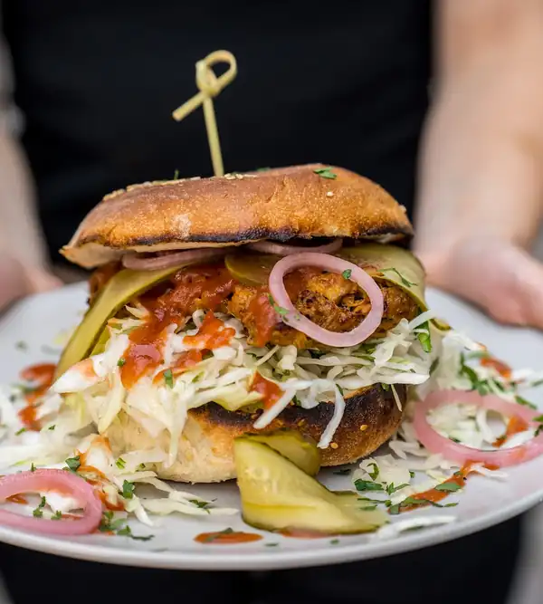 Burger z cebulą prażoną trzymany w dłoniach